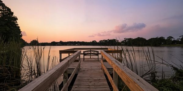 Wooden dock overlooking a calm lake at sunset with a bench.