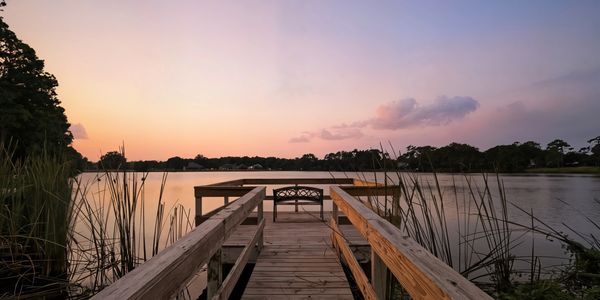 Wooden dock overlooking a calm lake at sunset with a bench.