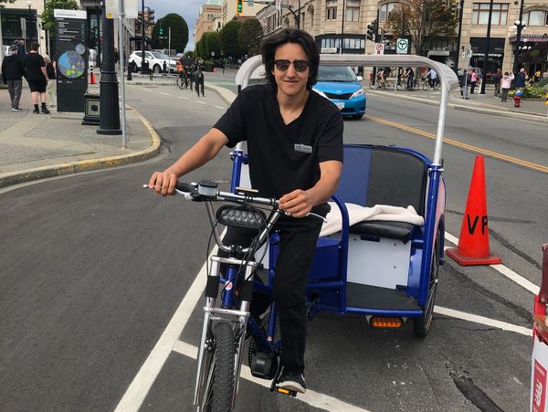 Man riding a pedicab on a city street with buildings and pedestrians.
