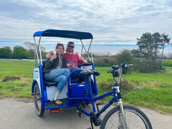 Two people enjoying ice cream on a blue pedicab in a green field.