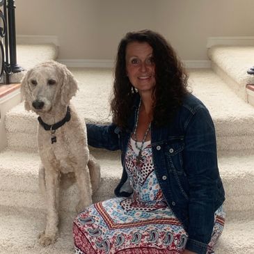 A woman sitting on carpeted stairs with a light-colored dog beside her.