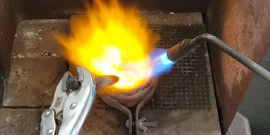 Metal is being mixed and melted with a torch.