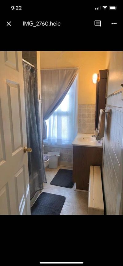 Small bathroom with shower, sink, and window with curtains.