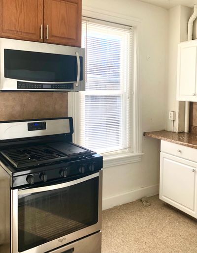 Modern kitchen corner with stove, microwave, and window.