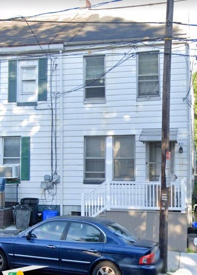 Blue sedan parked in front of a white two-story house with green shutters.
