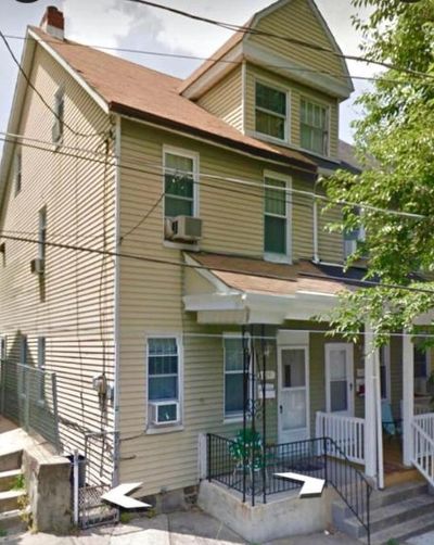 Two-story beige house with a small porch and air conditioner unit.