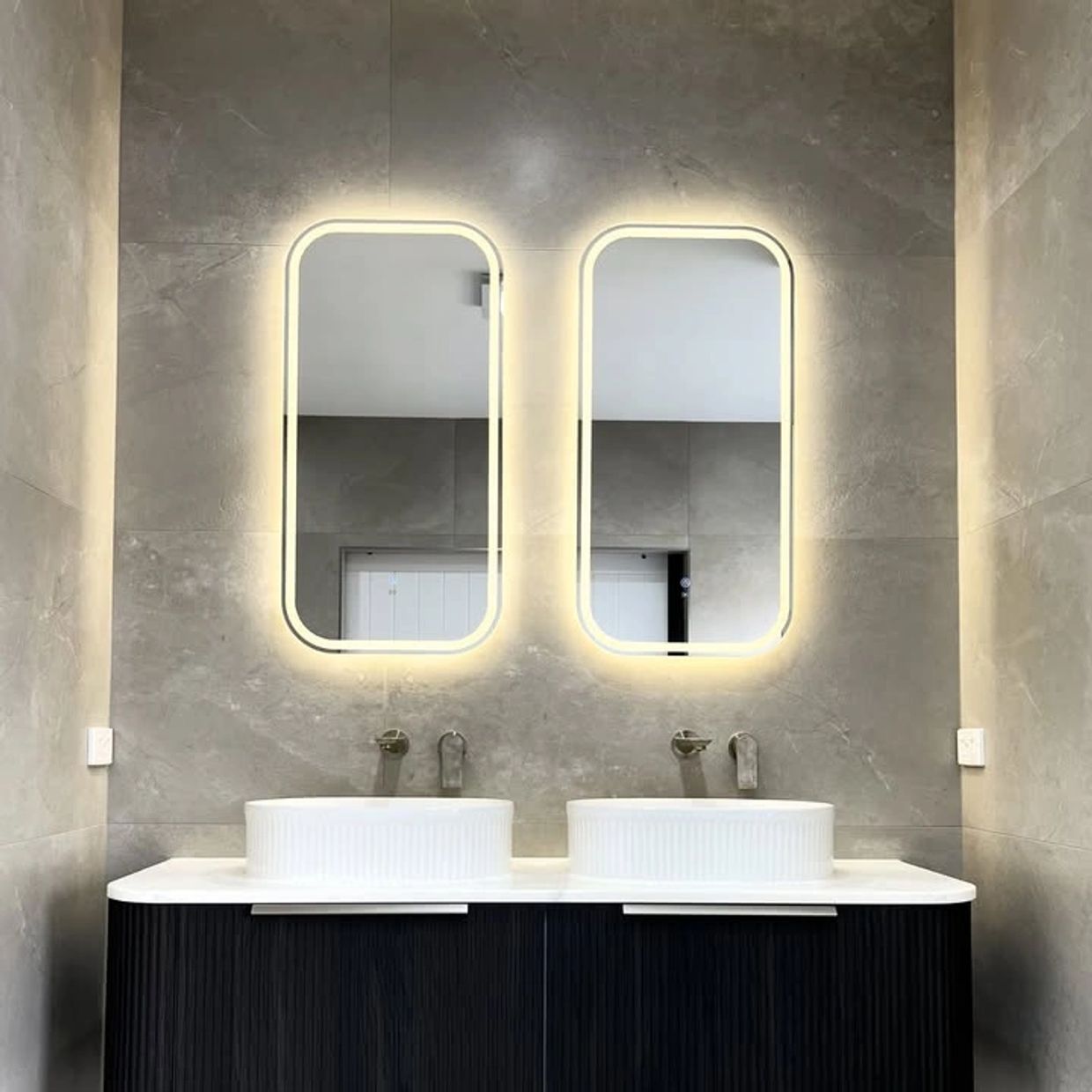 ARCOVE bathroom with twin basins, illuminated mirrors and a dark floating vanity.