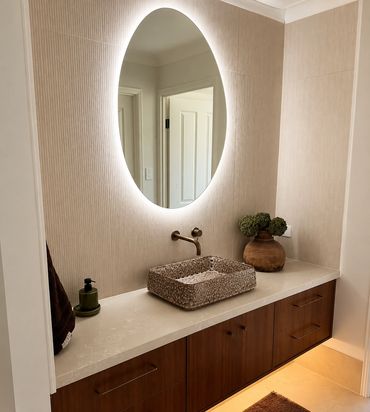 Bathroom vanity with a stone basin, timber cabinetry and an illuminated oval mirror.