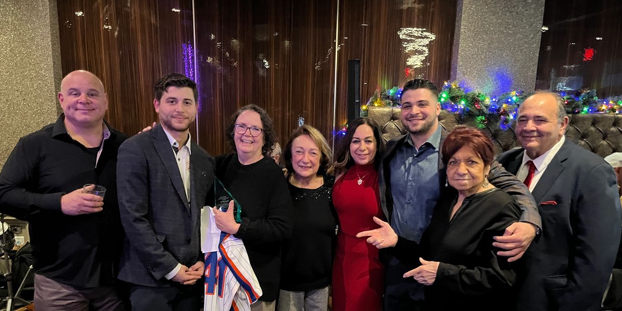 A group of eight people posing at a festive indoor gathering with holiday lights.