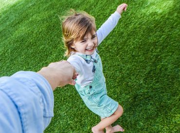 A child joyfully spins while holding an adult's hand on green grass.