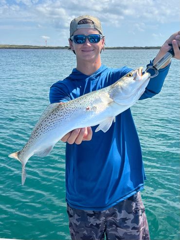 Young man proudly holding a large fish he caught on the water.
