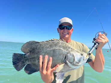 Man proudly holding a large fish on a sunny day by the water.