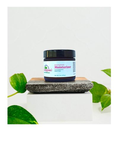 Jar of nighttime detoxifying moisturizer on display with green leaves.
