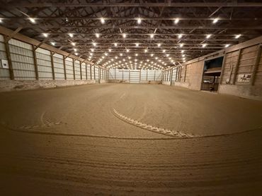 Large indoor arena with dirt floor and overhead lights.