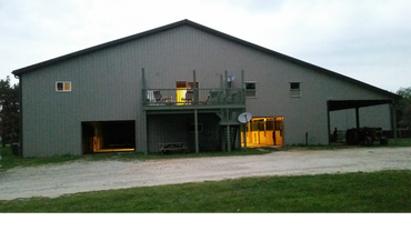 Large barn with lit interior and tractor outside at dusk.