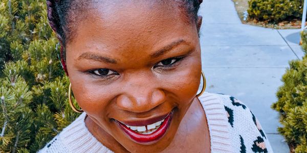 Close-up of a smiling woman with red lipstick outside.