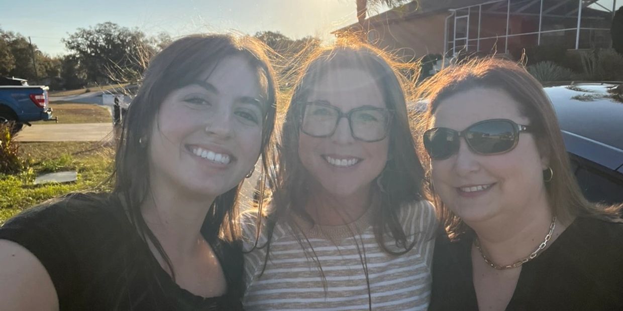 Three women smiling outdoors with the sun shining behind them.