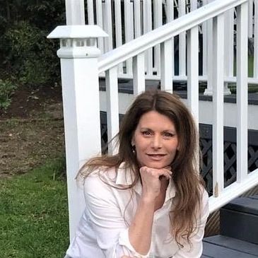 Woman in white shirt posing on outdoor steps with greenery background.