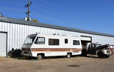 An old RV and a vintage truck parked beside a metal building under a clear blue sky.