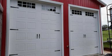 Two white garage doors on a red building with black handles and hinges.