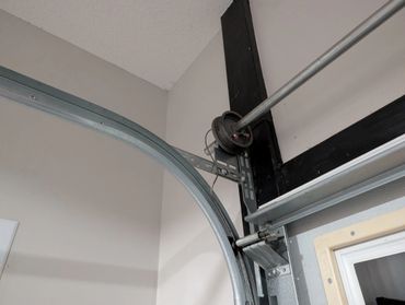 Close-up of a garage door pulley system with metal tracks and a black wooden support.
