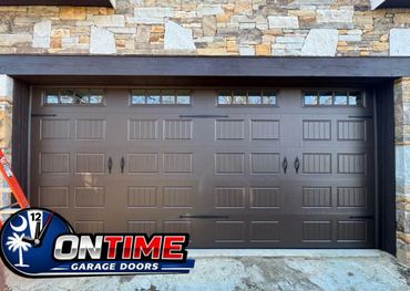 Brown garage door with decorative windows and handles, set in a stone wall.