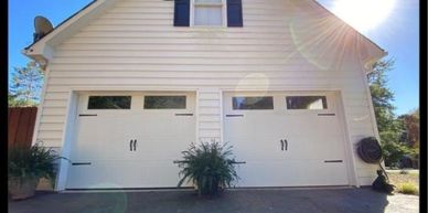 A white double garage door with plants in front and the sun shining.