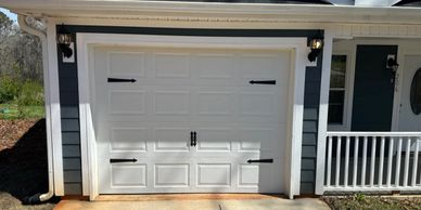 White garage door with decorative black hardware on a blue and white house.