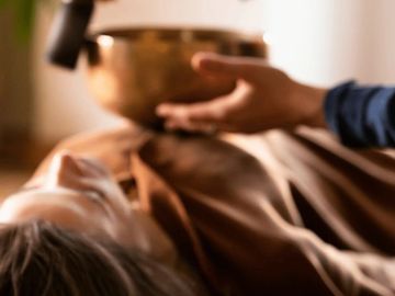 Person lying down with hand extended near a singing bowl, suggesting a healing session.