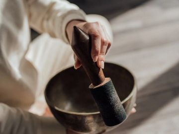 Hand holding a mallet over a singing bowl.
