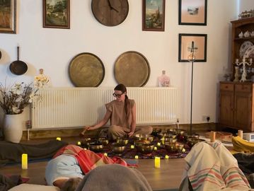 A woman meditates surrounded by candles and resting people in a cozy room.