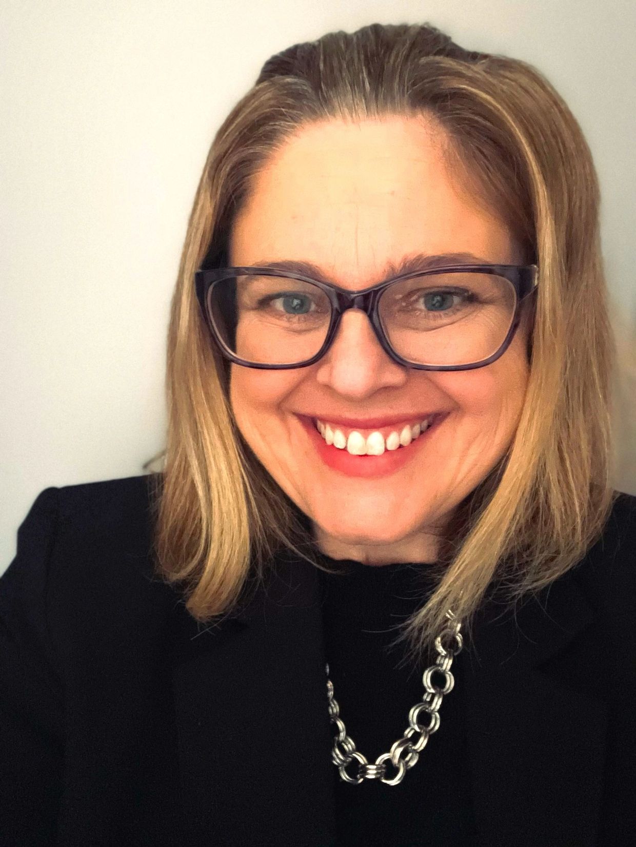 Smiling woman wearing glasses and a necklace.