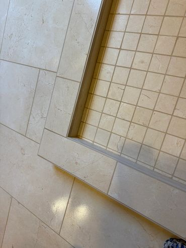 Beige tiled floor transitioning to a small square-tiled shower area.