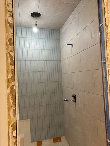 Bathroom under construction with tiled walls and exposed pipes.