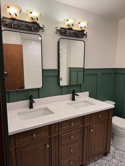 Bathroom with double sinks, green wainscoting, and decorative lighting. Bathroom remodeling services.