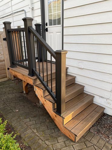 Wooden stairs with black railing leading to a white door outside a house.