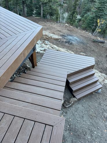 Wooden deck stairs leading down to a forested area with dirt ground.