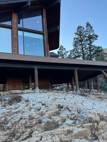 Modern house with large windows on rocky terrain surrounded by trees.