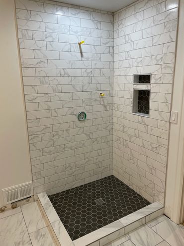 Modern shower with marble-patterned wall tiles and black hexagonal floor tiles.
