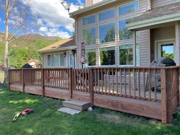 New wooden deck with railing outside a house on a sunny day.
