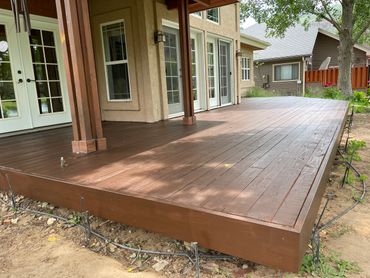 Large wooden deck attached to a house with brown stain and irrigation system around it.