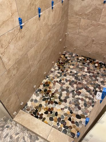 Shower area under renovation with pebble floor and beige tiled walls.