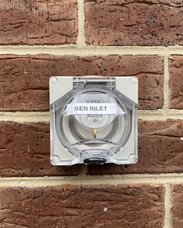 A generator inlet socket mounted on a brick wall.