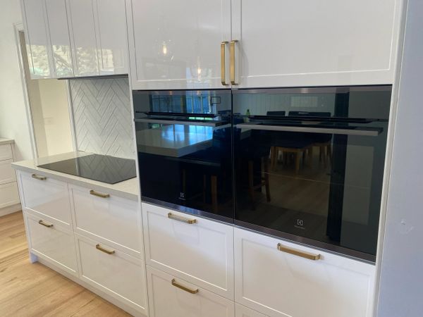 Modern kitchen with white cabinets, gold handles, and built-in Electrolux ovens.