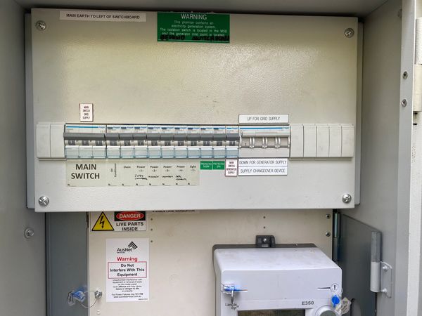 Electrical switchboard with labeled circuit breakers and safety warnings.