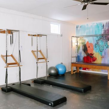 Bright Pilates studio with reformer machines and colorful wall art.