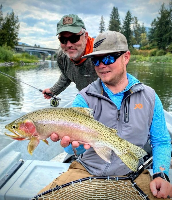 Clark Fork River Cutthroat Trout being held by Montana Fishing Guide with client behind him smiling