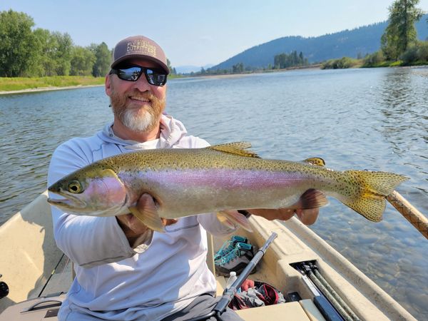 Clark Fork River Rainbow Trout being held by a Montana Fishing Guide in a drift boat with river behi