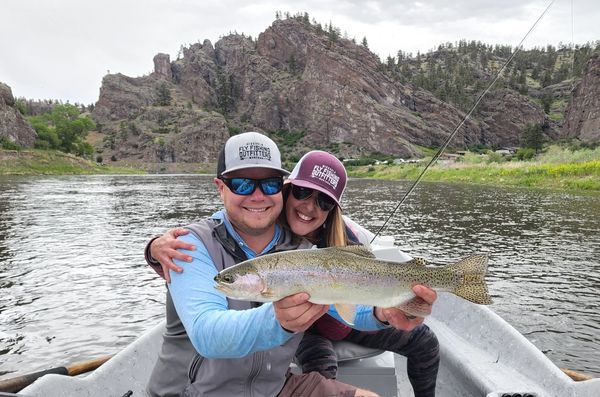 Rainbow trout being held by Montana Fishing Guide with woman client smiling and cliffs in distance