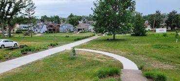 A suburban neighborhood with green lawns and a winding sidewalk under a cloudy sky.